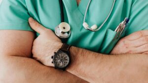A healthcare professional in green scrubs with a stethoscope and pens in the pocket, standing with arms crossed, representing the expertise of functional medicine doctors.